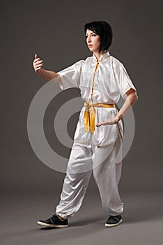 Young woman practicing tai chi chuan. Chinese management skill Qi`s energy. Gray background, studio shoot.