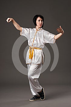 Young woman practicing tai chi chuan. Chinese management skill Qi`s energy. Gray background, studio shoot.