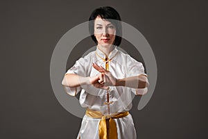 Young woman practicing tai chi chuan. Chinese management skill Qi`s energy. Gray background, studio shoot.