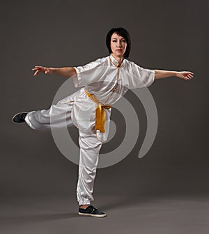 Young woman practicing tai chi chuan. Chinese management skill Qi`s energy. Gray background, studio shoot.