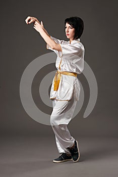 Young woman practicing tai chi chuan. Chinese management skill Qi`s energy. Gray background, studio shoot.