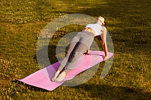 Young woman practicing yoga asana. Sporty brunette in sports clothes performs Purvottanasana exercise on background of