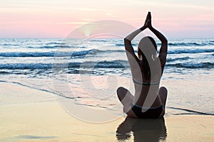 Young woman practicing yoga on the beach at amazing sunset.