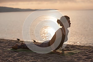 Young woman practicing yoga on the beach. cobra pose, Bhujangasana . Outdoors sports. Healthy living