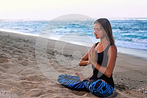 Young woman practicing yoga on the beach at sunrise