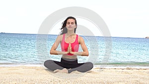 Young woman practicing yoga on the beach at sunset. Exercises calmness and harmony. Meditation in lotus pose. Healthy