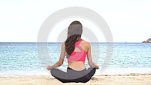 Young woman practicing yoga on the beach at sunset. Exercises calmness and harmony. Meditation in lotus pose. Healthy