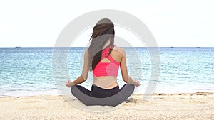 Young woman practicing yoga on the beach at sunset. Exercises calmness and harmony. Meditation in lotus pose. Healthy