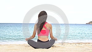 Young woman practicing yoga on the beach at sunset. Exercises calmness and harmony. Meditation in lotus pose. Healthy