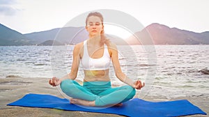 Young woman practicing yoga on the beach at sunset. Lotus pose