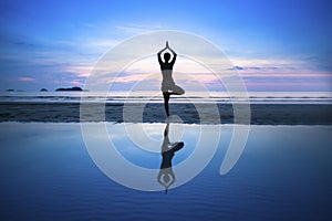Young woman practicing yoga on beach at surrealistic sunset.