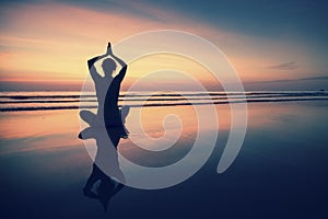 Young woman practicing yoga on beach at surrealistic sunset.