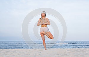 Young woman practicing yoga on the beach. Vrksasana pose