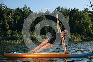 Young woman practicing yoga on color SUP board on river