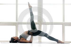 Young woman practicing yoga, doing Eka Pada Setu Bandha Sarvanga
