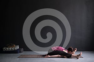 Young woman practicing yoga, doing Kurmasana, Tortoise posture, Turtle Pose