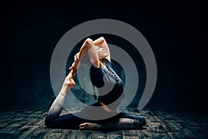 Young woman practicing yoga doing one legged king pigeon pose in dark room