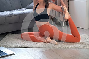 Young woman is practicing yoga doing pigeon pose at home online training.