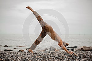 Young woman practicing yoga in downward facing dog pose on beach