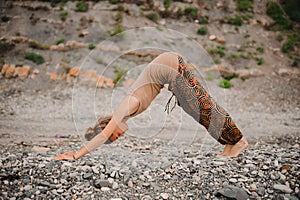 Young woman practicing yoga in downward facing dog pose on beach