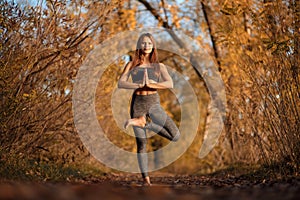 Young woman practicing yoga exercise in autumn park with yellow leaves. Sports and recreation lifestyle