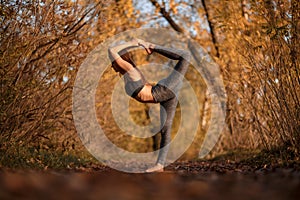 Young woman practicing yoga exercise in autumn park with yellow leaves. Sports and recreation lifestyle