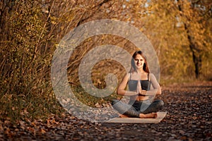 Young woman practicing yoga exercise in autumn park with yellow leaves. Sports and recreation lifestyle