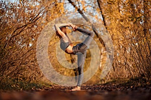 Young woman practicing yoga exercise in autumn park with yellow leaves. Sports and recreation lifestyle