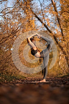 Young woman practicing yoga exercise at autumn park with yellow leaves. Sports and recreation lifestyle