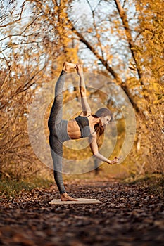 Young woman practicing yoga exercise at autumn park with yellow leaves. Sports and recreation lifestyle