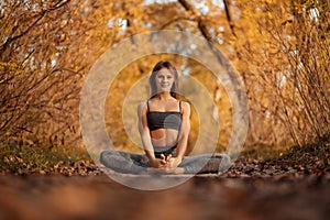 Young woman practicing yoga exercise at autumn park with yellow leaves. Sports and recreation lifestyle