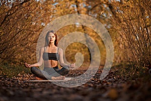 Young woman practicing yoga exercise at autumn park with yellow leaves. Sports and recreation lifestyle