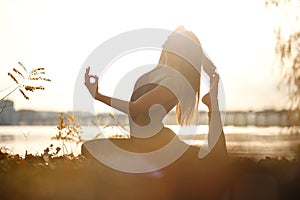 Young woman practicing yoga exercise at river beach and city background