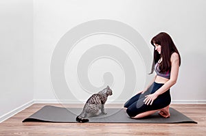 Young Woman Practicing Yoga At Home and Play with Cat on a Mat