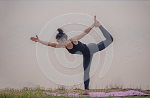 Young woman is practicing yoga at a lakeside garden.