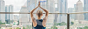Young woman is practicing yoga in the morning on her balcony with a panoramic view of the city and skyscrapers BANNER