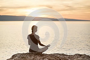 Young woman practicing yoga near the sea at sunset. Harmony, meditation and travel concept. Healthy lifestyle