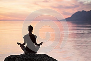 Young woman practicing yoga near the sea at sunset. Harmony, meditation and travel concept. Healthy lifestyle