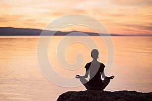 Young woman practicing yoga near the sea at sunset. Harmony, meditation and travel concept. Healthy lifestyle