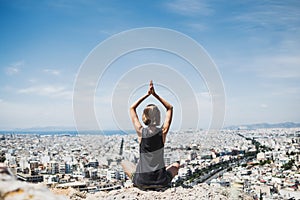 Young woman practicing yoga outdoors with a big city at the background