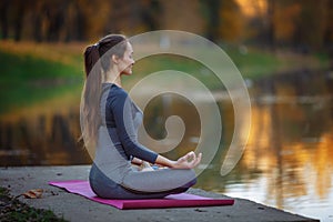 Young woman practicing yoga outdoors. Female meditate outdoor infront of beautiful autumn nature.