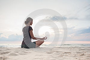 Young woman practicing yoga outdoors. Girl meditating with sunset sea view at background