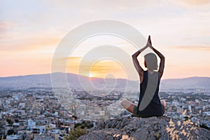 Young woman practicing yoga outdoors at sunset with a big city at the background. Harmony, meditation and healthy lifestyle concep