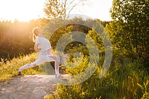 Young woman practicing yoga and performing Peaceful Warrior Pose outside in park evening, sunlight.