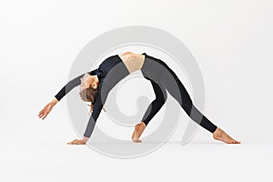 A young woman practicing yoga performs the exercise of Kamatkarasana, the pose of a dancing dog, trains in black sportswear