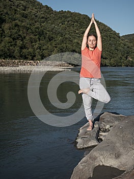 Young woman is practicing yoga in pose at mountain lake