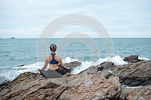 Young woman practicing yoga on a rock at the beach