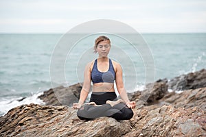 Young woman practicing yoga on a rock at the beach