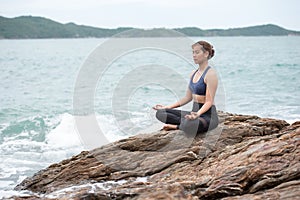 Young woman practicing yoga on a rock at the sea
