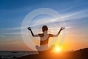 Young woman practicing yoga on the sea beach during amazing sunset.